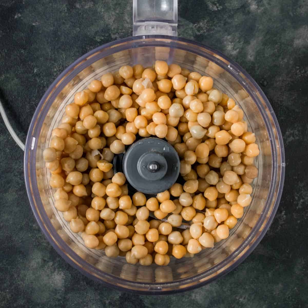 składniki hummusu w blenderze ciecierzyca z tahini, czosnkiem i cytryną w szklanym blenderze