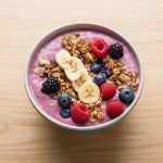 szklanka zielonego smoothie z bananami jagodami i erytrytolem obok blendera