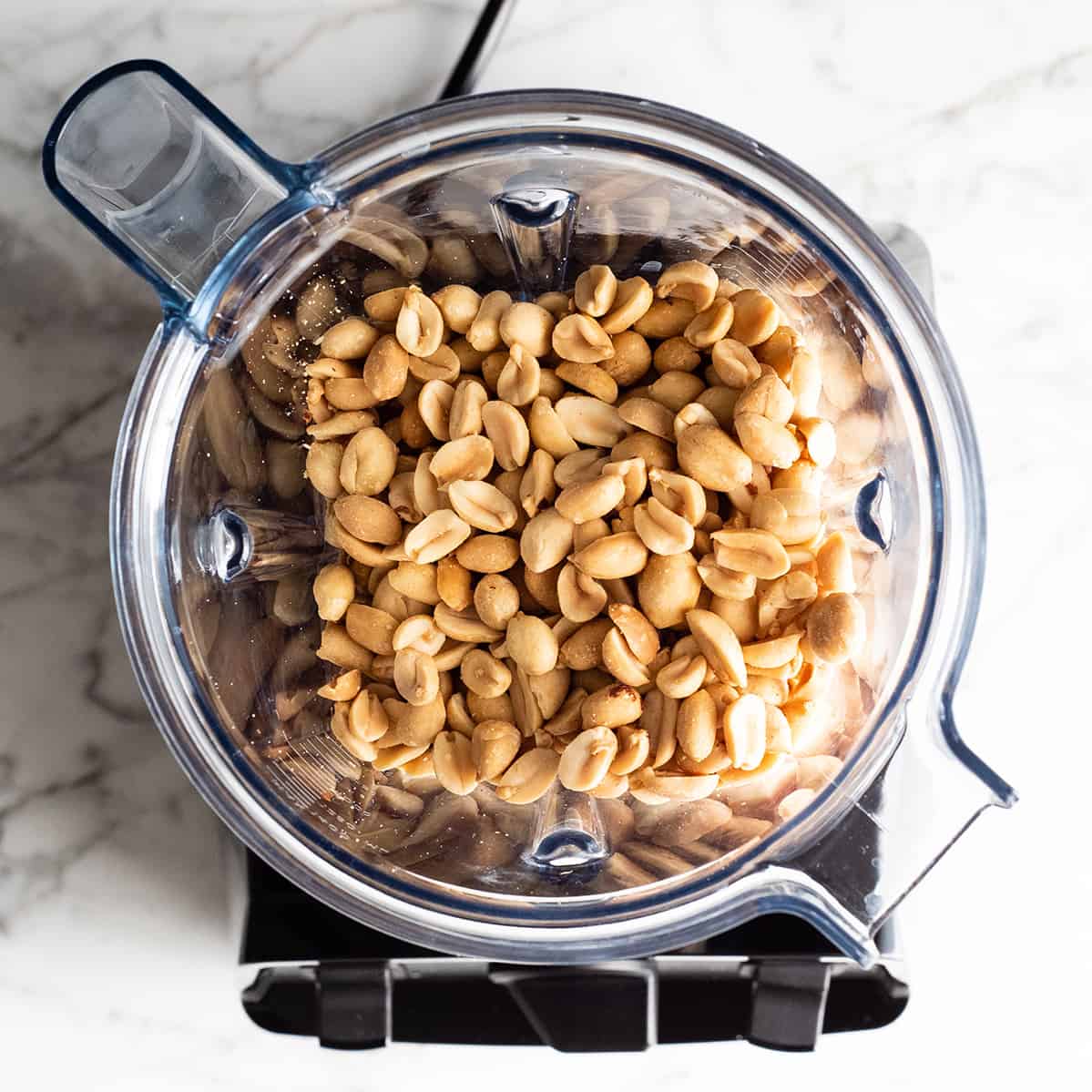 Blender stołowy z prażonymi orzechami ziemnymi obok słoika gładkiego masła orzechowego