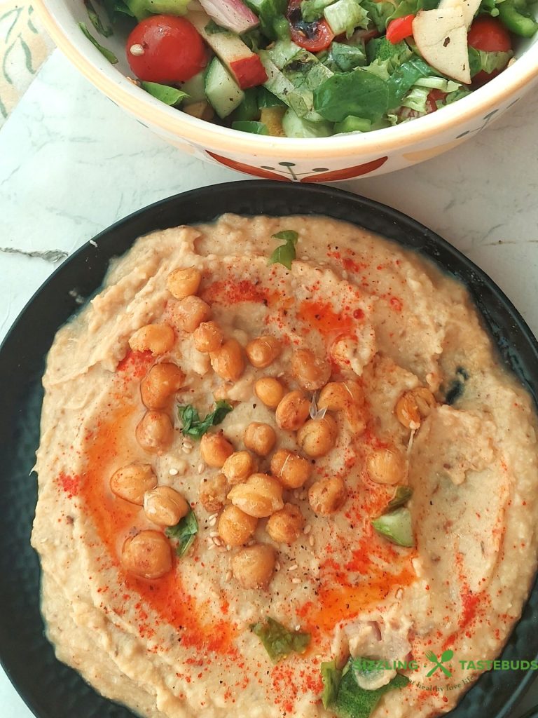 hummus na talerzu polany oliwą z pietruszką i papryką obok