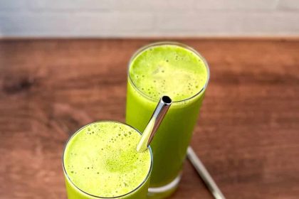 Zielony koktajl z pietruszką w szklance obok świeżych liści i owoców na stole